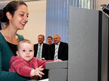 NEPS-Mitarbeiterin Kerstin Hoenig demonstrierte am Donnerstag mit ihrer Tochter Ida Marlen, wie Babys für das Nationale Bildungspanel getestet werden. Auch der bayerische Wissenschaftsminister Wolfgang Heubisch (hinten links) schaute zu. Foto: Matthias Hoch