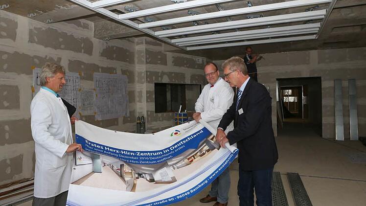 Die Chefärzte Peter Rieckmann und Martin Braun begehen gemeinsam mit Wolfgang Freitag (Leiter Bau und Technik), regelmäßig die Baustelle. Noch müssen sie sich anhand eines Plakats vorstellen, wie das Herz-Hirn-Zentrum einmal aussehen soll. Foto: Barbara Herbst